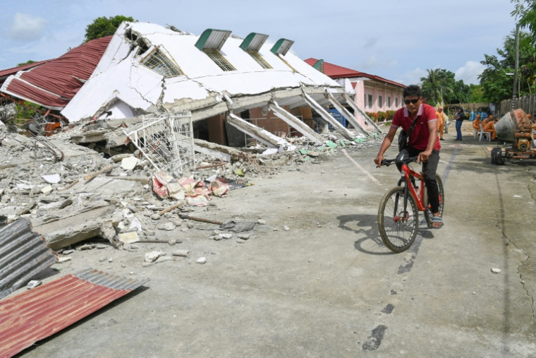 Un homme passe à vélo devant un bâtiment effondré où trois personnes ont été retrouvées mortes après un séisme à Bogo, dans la province de Cebu aux Philippines, le 2 octobre 2025 ( AFP / Ted ALJIBE )