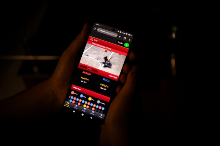 Sur cette photo prise le 15 juillet 2025, Jay, un artiste graphiste de 24 ans qui a requis l'anonymat, montre durant quelques secondes aux journalistes de l'AFP un combat de coqs en direct sur son téléphone, dans la province de Bulacan, en banlieue de Manille ( AFP / Ted ALJIBE )