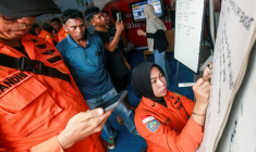 Des proches de personnes disparues regardent une employée de l'agence de recherche et de secours indonésienne écrire des informations sur les opérations en cours après le naufrage d'un ferry, le 13 septembre 2026 à Banjarmasin en Indonésie ( AFP / INFUZ )