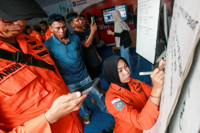 Des proches de personnes disparues regardent une employée de l'agence de recherche et de secours indonésienne écrire des informations sur les opérations en cours après le naufrage d'un ferry, le 13 septembre 2026 à Banjarmasin en Indonésie ( AFP / INFUZ )
