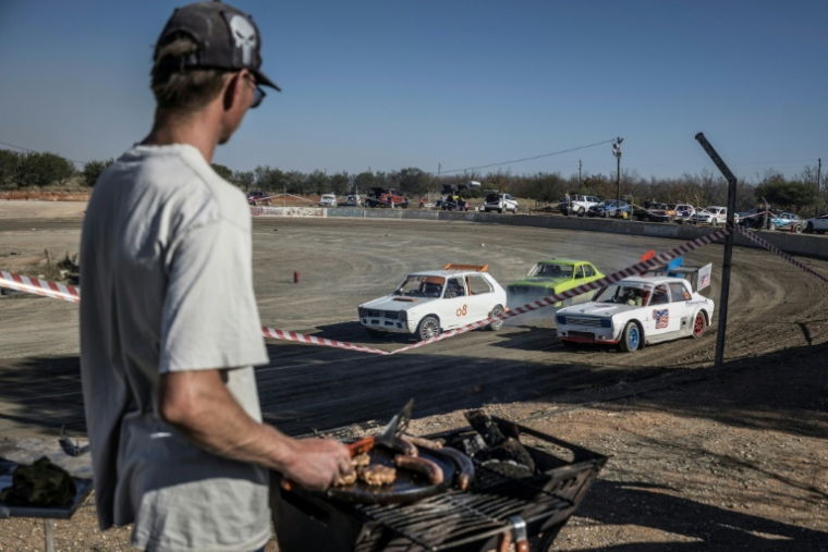 Un spectateur grille de la viande sur un braai (barbecue) devant une course de voiture sur l'ovale de terre de l'enclave afrikane en Afrique du Sud, le 30 mai 2026. ( AFP / MARCO LONGARI )