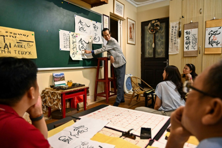 Le calligraphe Nguyen Thanh Tung (c) enseigne la calligraphie à des étudiants, chez lui à Hanoï, le 15 mai 2025 au Vietnam ( AFP / Nhac NGUYEN )