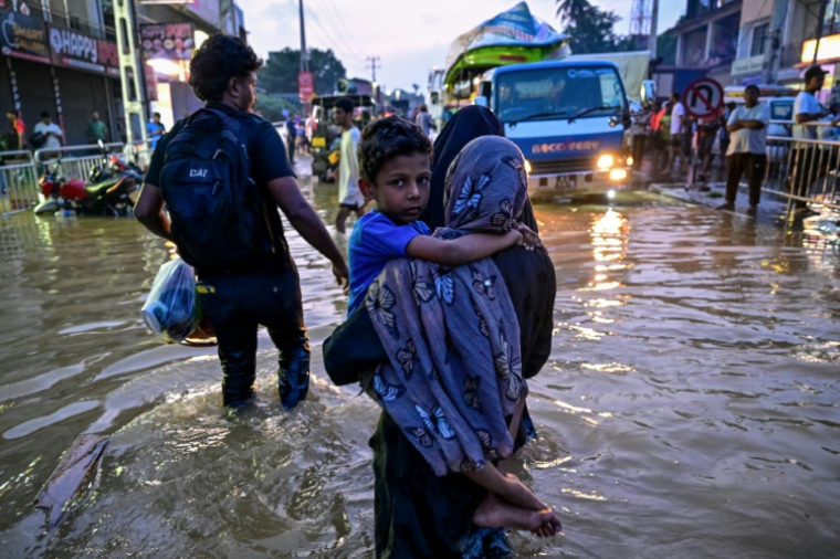 Une femme portant un enfant traverse une rue inondée après de fortes pluies à Wellampitiya, au Sri Lanka, près de Colombo, le 30 novembre 2025 ( AFP / Ishara S. KODIKARA )