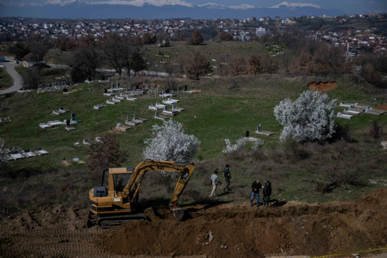 Des experts médico-légaux devant un engin de chantier qui fouille un terrain dans le cadre des recherches liées aux personnes disparues de la guerre du Kosovo, près de la ville de Rahovec, le 11 mars 2026 ( AFP / Armend NIMANI )