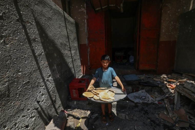 Un garçon palestinien sort avec du pain d'une boulangerie de fortune touchée par des frappes israéliennes dans le camp de réfugiés de Nusseirat, dans le centre de la bande de Gaza, le 8 mai 2025 ( AFP / Eyad BABA )