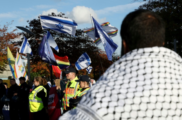 Un militant propalestinien (de dos) observe des contre-manifestants brandissant des drapeaux israéliens en marge d’une manifestation de soutien aux Palestiniens, à Berlin, le 10 octobre 2026 ( AFP / Adam BERRY )
