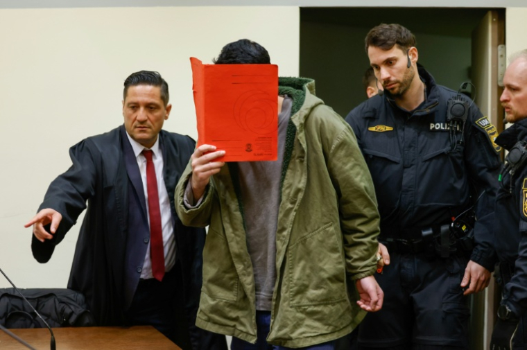 L'Afghan Farhad N., le visage caché derrière un dossier, arrive au tribunal avec son avocat Omer Sahinci (g), le 16 janvier 2026 à Munich, pour le début de son procès pour avoir foncé en voiture dans la foule à Munich en 2025  ( AFP / Michaela Stache )