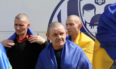 Photo diffusée par le Quartier général de coordination pour le traitement des prisonniers de guerre, le 19 août 2026, montrant d'anciens prisonniers de guerre ukrainiens, enveloppés dans des drapeaux nationaux, près d'un bus après un échange effectué dans un lieu tenu secret ( Quartier général de coordination pour le traitement des prisonniers de guerre / Handout )