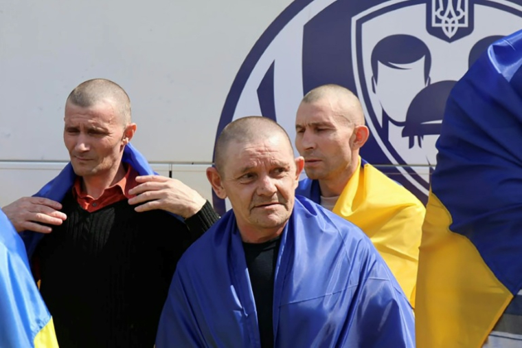 Photo diffusée par le Quartier général de coordination pour le traitement des prisonniers de guerre, le 19 août 2026, montrant d'anciens prisonniers de guerre ukrainiens, enveloppés dans des drapeaux nationaux, près d'un bus après un échange effectué dans un lieu tenu secret ( Quartier général de coordination pour le traitement des prisonniers de guerre / Handout )