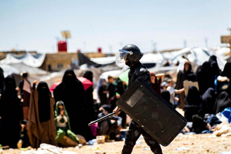 Un membre des forces de sécurité kurdes syriennes Asayish devant des proches de combattants présumés de l’État islamique (EI) dans le camp d’al-Hol, administré par les Kurdes, au nord-est de la Syrie, le 18 avril 2025 ( AFP / Delil SOULEIMAN )