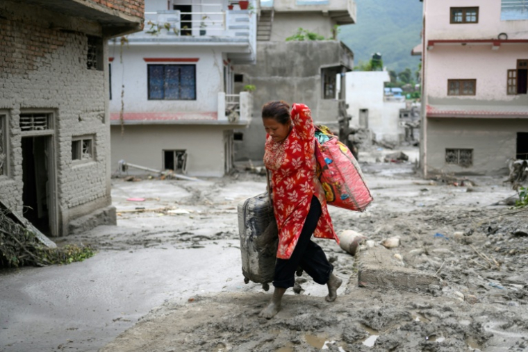 Une femme transporte des effets personnels qu'elle a pu sauver après la crue destructrice qui a fait au moins 633 morts à la frontière entre le Népal et la Chine, le 28 août 2026 dans le district népalais de Nuwakot   ( AFP / MANAN VATSYAYANA )