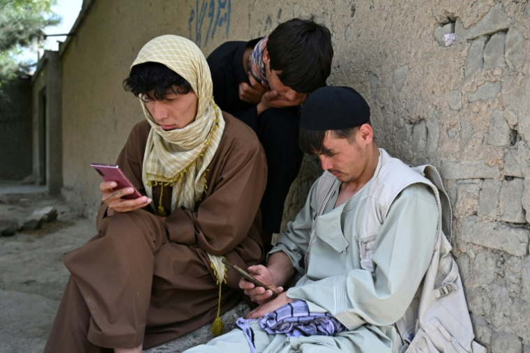 Des jeunes Afghans consultent leurs smartphones à Kaboul, le 10 août 2026 ( AFP / Wakil KOHSAR )