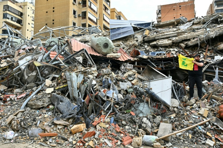 Un homme dans des décombres tient un drapeau du Hezbollah tandis que des personnes déplacées retournent dans leur quartier de la banlieue sud de Beyrouth après l'entrée en vigueur d'un cessez-le-feu de 10 jours avec Israël, le 17 avril 2026 au Liban ( AFP / FADEL itani )
