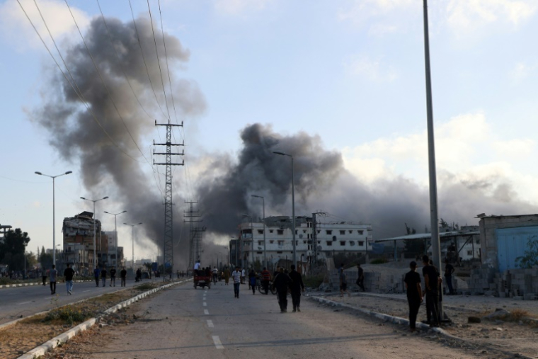 De la fumée lors d'une frappe israélienne alors que des Palestiniens marchent sur une route utilisée pour atteindre un point de distribution d'aide de la Fondation humanitaire de Gaza (GHF,) près du camp de réfugiés de Nousseirat, dans le centre de la bande de Gaza, le 25 juin 2025 ( AFP / Eyad BABA )