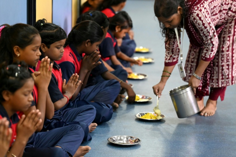 Des élèves en prières avant un petit déjeuner à "l'école du feu rouge", qui accueille des enfants défavorisés dans des conteneurs aménagés en salles de cours sous un pont autoroutier, le 18 mai 2026 à Bombay ( AFP / Punit PARANJPE )