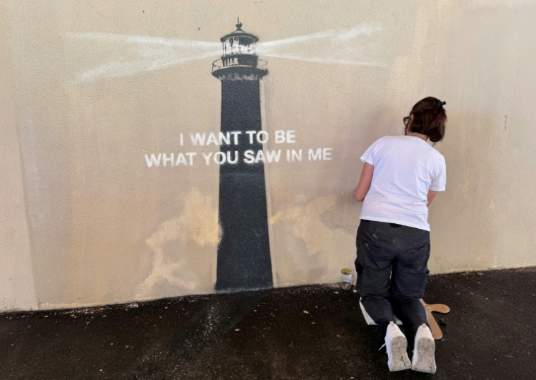 Agnès Perrone, peintre en décor du patrimoine, répare une œuvre d'art de l'artiste de rue Banksy représentant un phare sur la façade d'un bâtiment, après qu'elle a été vandalisée pendant la nuit à Marseille, le 1er juin 2025 ( AFP / Viken KANTARCI )