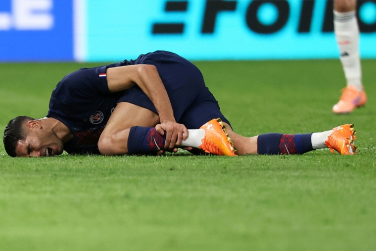 Le défenseur marocain du PSG Achraf Hakimi se tord de douleur après un mauvais tacle de l'ailier du Bayern Munich Luis Diaz, lors de l'affrontement de Ligue des champions au Parc des Princes le 4 novembre 2025 ( AFP / Anne-Christine POUJOULAT )
