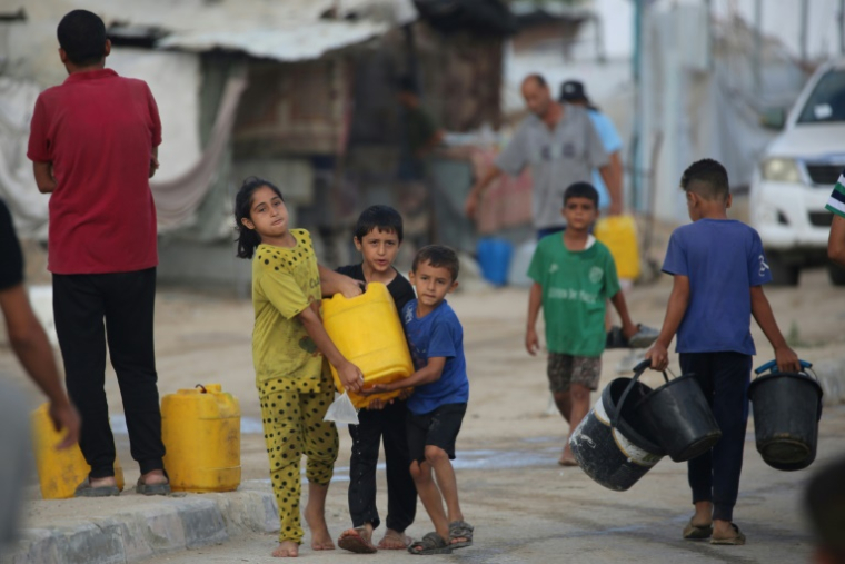 Des enfants palestiniens portent un bidon rempli d'eau potable à partir de citernes mobiles dans le camp de réfugiés de Bureij, dans le centre de la bande de Gaza, le 6 octobre 2025 ( AFP / Eyad BABA )