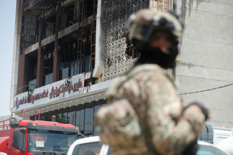 Un membre des forces de sécurité irakiennes devant la façade incendiée du centre commercial Hyper Mall de Kut, dans l'est de l'Irak, le 17 juillet 2025 ( AFP / AHMAD AL-RUBAYE )