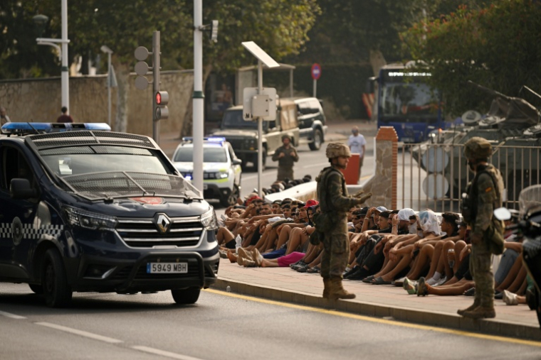 Des soldats espagnols surveillent des migrants assis sur le trottoir avant de les escorter de nouveau vers le Maroc, dans l’enclave espagnole de Ceuta, en Afrique du Nord, le 1er août 2026 ( AFP / JORGE GUERRERO )