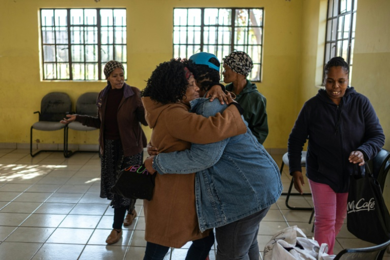 Baile Bantseke (c,g), grand-mère d'un enfant autiste, enlace Lilly Stebe (c,d), mère adoptive d'une enfant atteinte de paralysie cérébrale, lors d'une réunion du Snake Park Cerebral Palsy Forum à Soweto, le 23 mai 2025 en Afrique du Sud ( AFP / EMMANUEL CROSET )