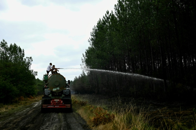 Des agriculteurs aspergent d'eau des points chauds pour aider les pompiers à combattre l'incendie à Saint-Jean-d'Illac, à l'ouest de Bordeaux, le 27 juillet 2026 ( AFP / Philippe Lopez )