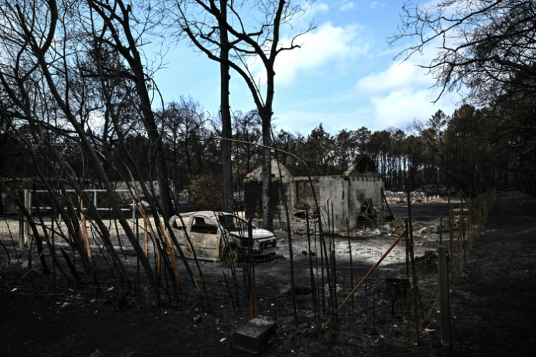 Une voiture calcinée devant une maison détruite par les flammes, le 3 août 2026 au Porge, en Gironde  ( AFP / Christophe ARCHAMBAULT )