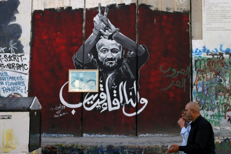 Des hommes marchent devant un portrait du dirigeant palestinien Marwan Barghouti peint sur la barrière séparant la Cisjordanie occupée d'Israël le 6 novembre 2023 à Bethléem.  ( AFP / HAZEM BADER )