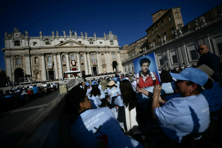 A faithful holds a portrait of late teenager Carlo Acutis in front of Saint Peter's Basilica ahead of a Holy Mass and canonisation ceremony of Blessed Carlo Acutis and Pier Giorgio Frassati in St Peter's Square at the Vatican on September 7, 2025. An Italian teenager dubbed "God's Influencer" for his efforts to spread the Catholic faith online will become the first millennial saint Sunday at a canonisation attended by thousands of pilgrims. Computer whiz Carlo Acutis, who died of leukemia in 2006 aged 15, will be raised to sainthood by Pope Leo XIV in a solemn ceremony in St Peter's Square at the Vatican. Italian Pier Giorgio Frassati, a mountaineering enthusiast who died in 1925 and was known for his social and spiritual commitment, will also be made a saint on September 7, 2025. ( AFP / Filippo MONTEFORTE )