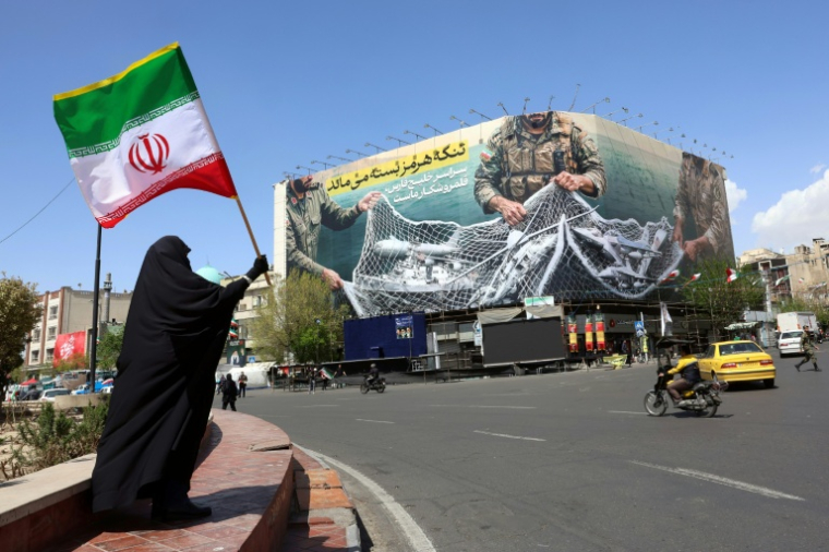Une femme tient le drapeau iranien près d'une affichage géante "Le détroit d'Ormuz reste fermé", le 5 avril 2026 à Téhéran ( AFP / - )